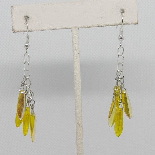 Yellow leaf-shaped earrings on a white stand against a light gray background