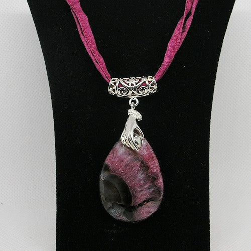 Necklace with a pink and black stone pendant on a black stand.