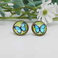 Butterfly-themed stud earrings on a white background with greenery and flowers.