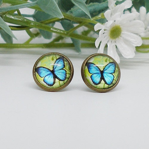 Butterfly-themed stud earrings on a white background with greenery and flowers.