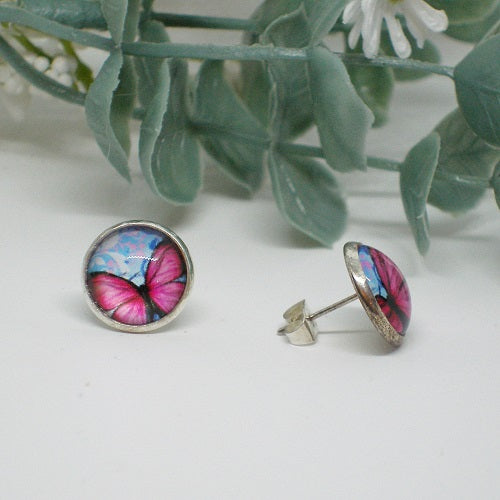 Butterfly-themed stud earrings on a white surface with green leaves in the background