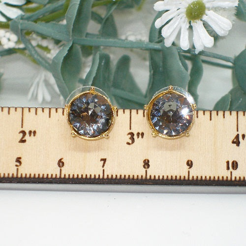 Gold earrings with crystals on a ruler for scale, with flowers in the background