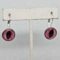 Earrings with purple and pink eye-like design on a white stand against a gray background
