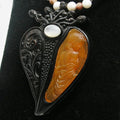 Decorative pendant with black filigree, amber-colored stone, and white bead on a black background