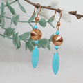 Pair of earrings with turquoise stones and copper accents on a branch with leaves.
