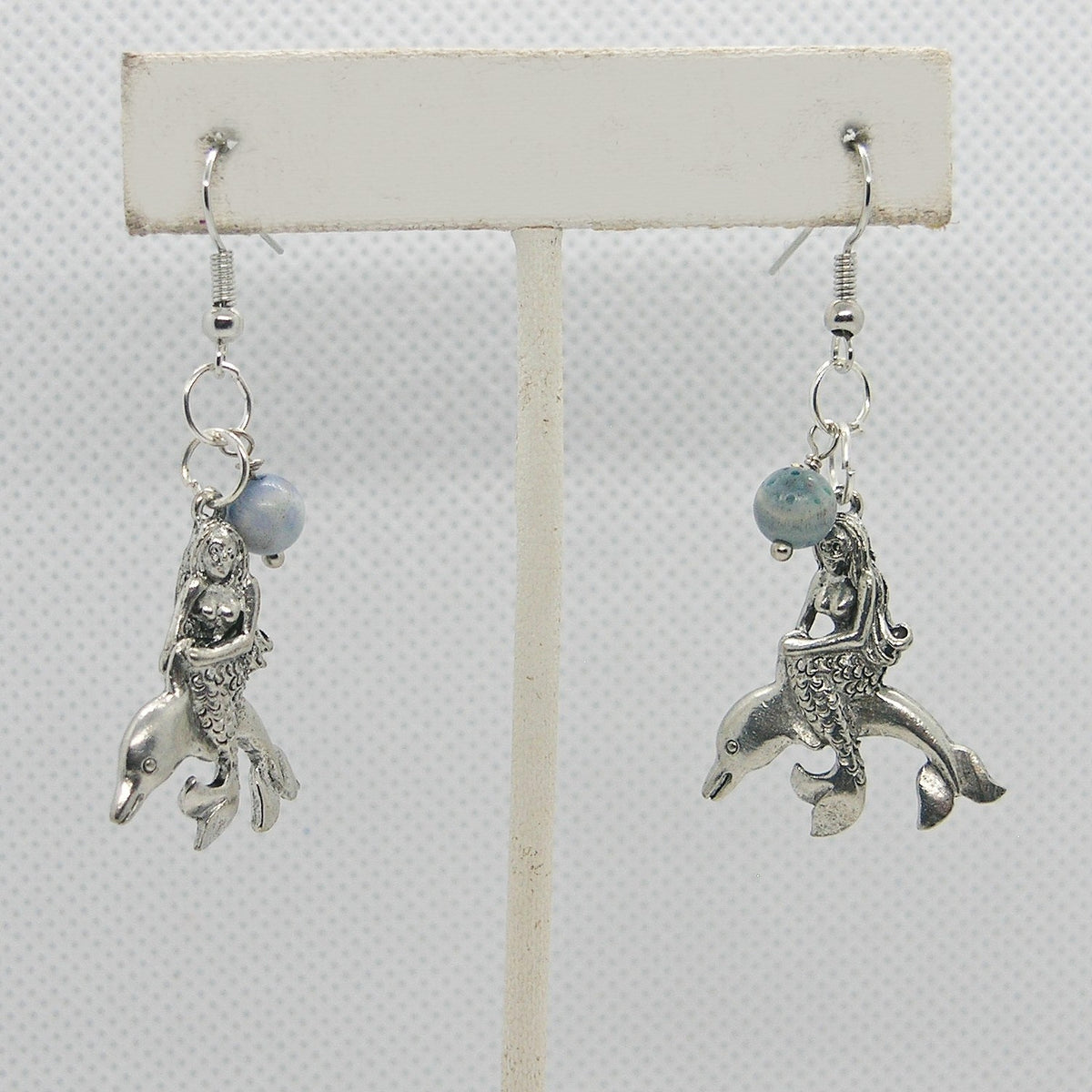 Pair of silver mermaid and dolphin earrings on a white background