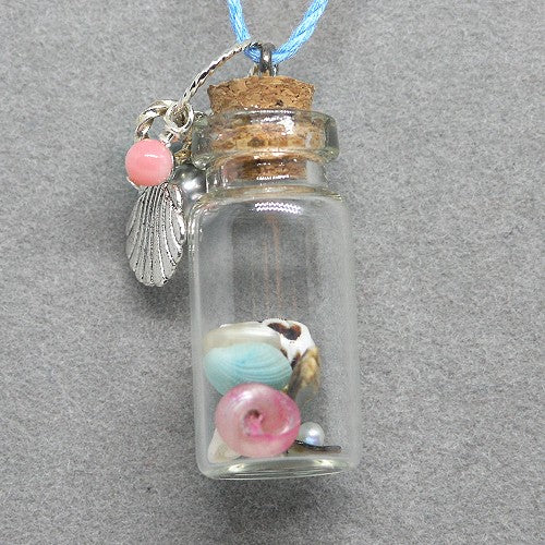 Glass bottle pendant with cork lid containing small shells and a pink bead, on a gray background