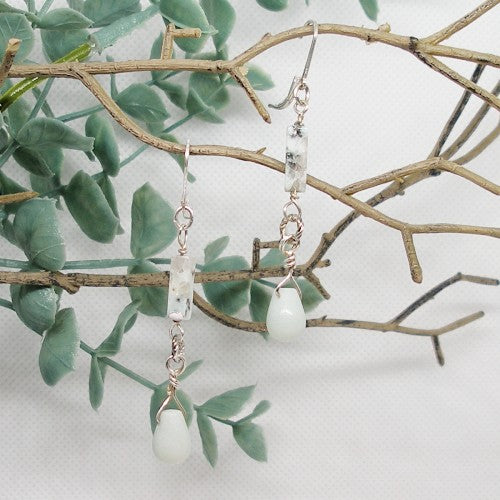 Pair of pastel color earrings hanging on a branch with green leaves.