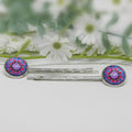 Silver hair pins with colorful circular ends on a white surface with flowers in the background