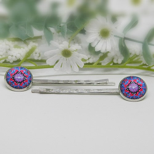Silver hair pins with colorful circular ends on a white surface with flowers in the background