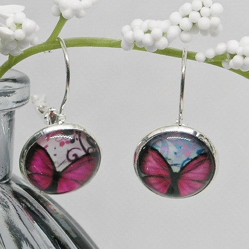 Butterfly-themed earrings hanging from a branch with white flowers.