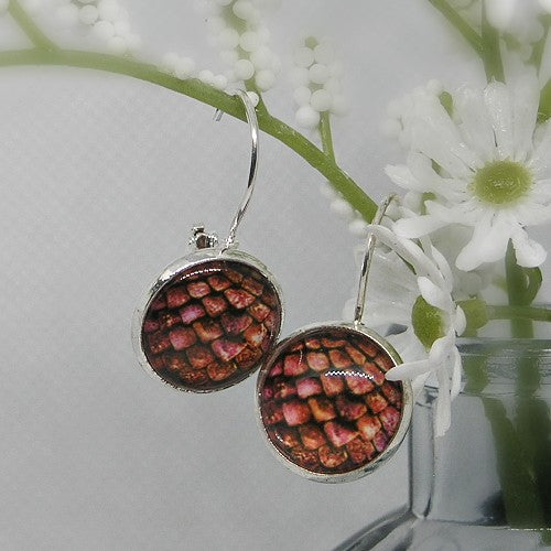 Pair of earrings with a snake scale pattern on a white background with flowers.