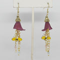 Pair of earrings with purple flower-like elements and gold bee accents on a white stand.