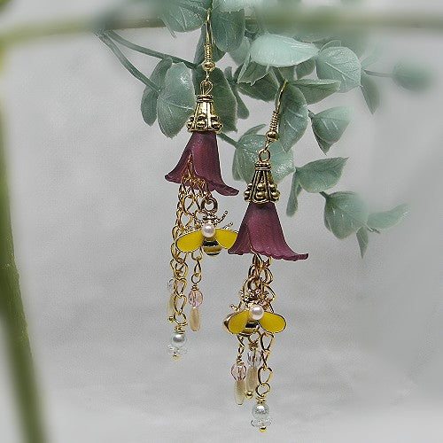 Earrings with floral designs and gold bee accents hanging on a branch with leaves.