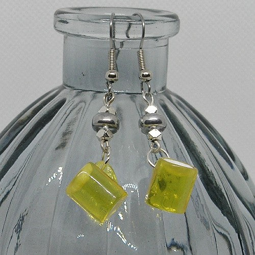 Yellow mug shaped earrings with silver hooks on a clear glass bottle.