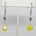 Yellow mug-shaped earrings on a white stand with a light gray background