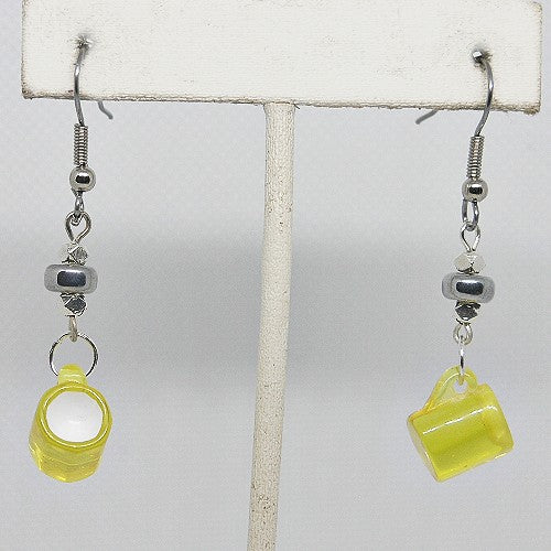 Yellow mug-shaped earrings on a white stand with a light gray background