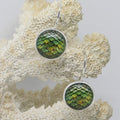 Green and silver earrings on a textured beige surface