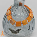 Bracelet with orange beads and a butterfly charm on a gray background