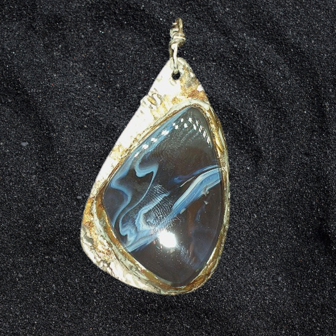Teardrop-shaped pendant with blue marbled design and gold edge on a black background