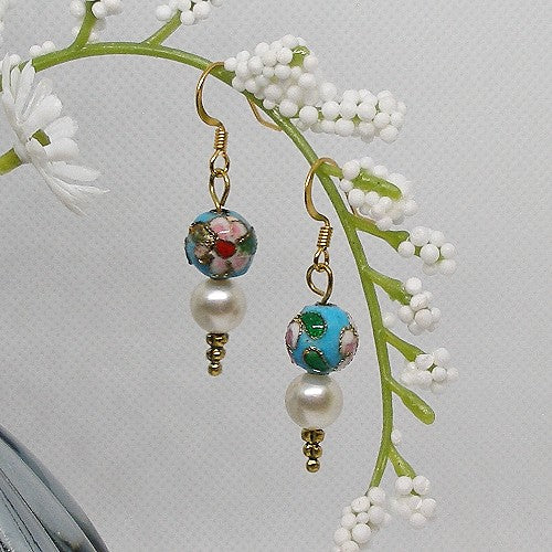 Pair of earrings with floral and pearl design hanging on a branch with white flowers.