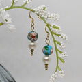 Pair of earrings with floral and pearl design hanging on a branch with white flowers.