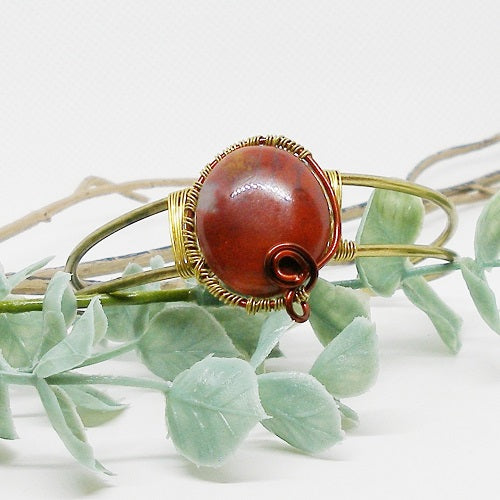 Bangle with a red stone and gold wire wrapping on green leaves