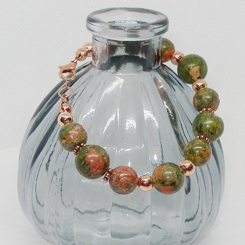 Beaded bracelet with green and copper beads on a clear glass bottle