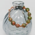Beaded bracelet with green and copper beads on a clear glass bottle