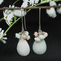 Pair of earrings with white teardrop stones and pink beads hanging on a branch with white flowers.