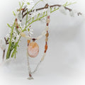 Necklace with a large peach colored stone pendant on a branch with white flowers