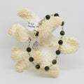Green and Black beaded bracelet on a piece of coral against a white background