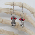 Silver heart earrings with red beads on a branch against a white background