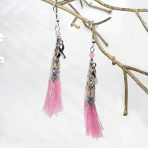 Pink tassel earrings hanging from a branch on a light background
