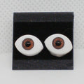 Pair of plastic eyes with brown pupils on a black display stand against a gray background