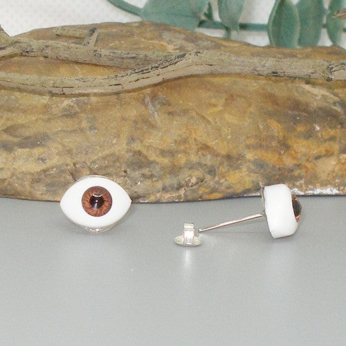 Eyeball-shaped earrings on a gray surface with a rock in the background
