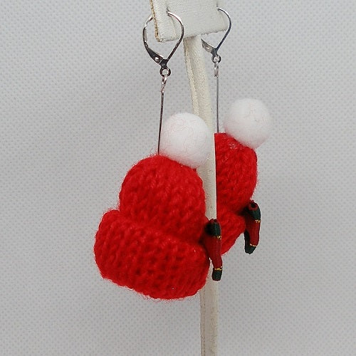 Red knitted ski hat earrings with white poms on a gray background

