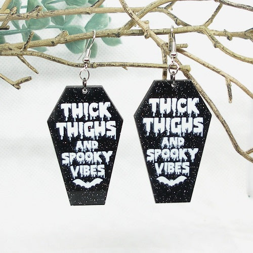 Black coffin-shaped earrings with white text and designs on a branch background