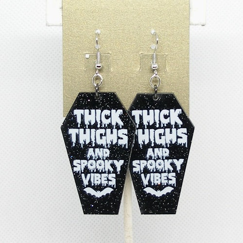 Black coffin-shaped earrings with white text on a beige card