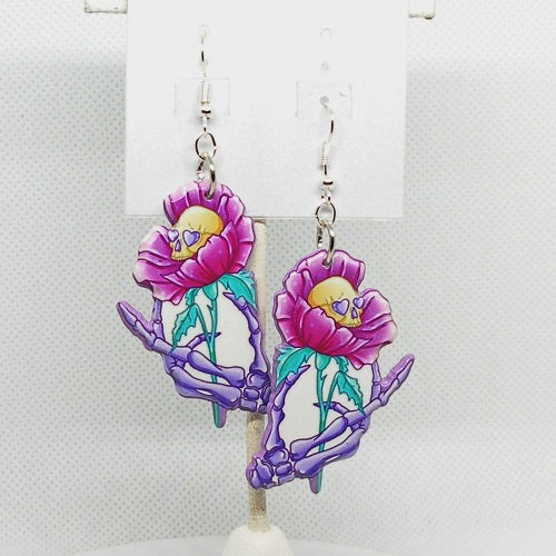 Pair of earrings with pink flowers and purple skeletons on a white background