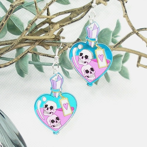 Heart-shaped earrings with skull designs on a white background with green leaves.
