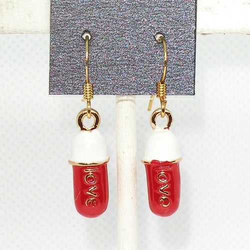 Red and white capsule-shaped earrings with 'LOVE' engraving on a gray card.