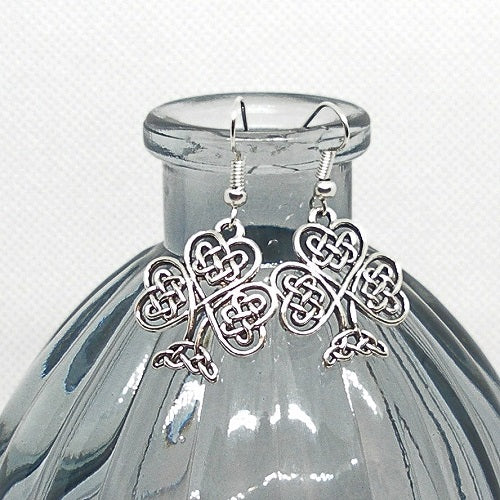 Silver Celtic knot earrings on a clear glass bottle with a white background