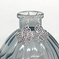 Silver Celtic knot earrings on a clear glass bottle with a white background
