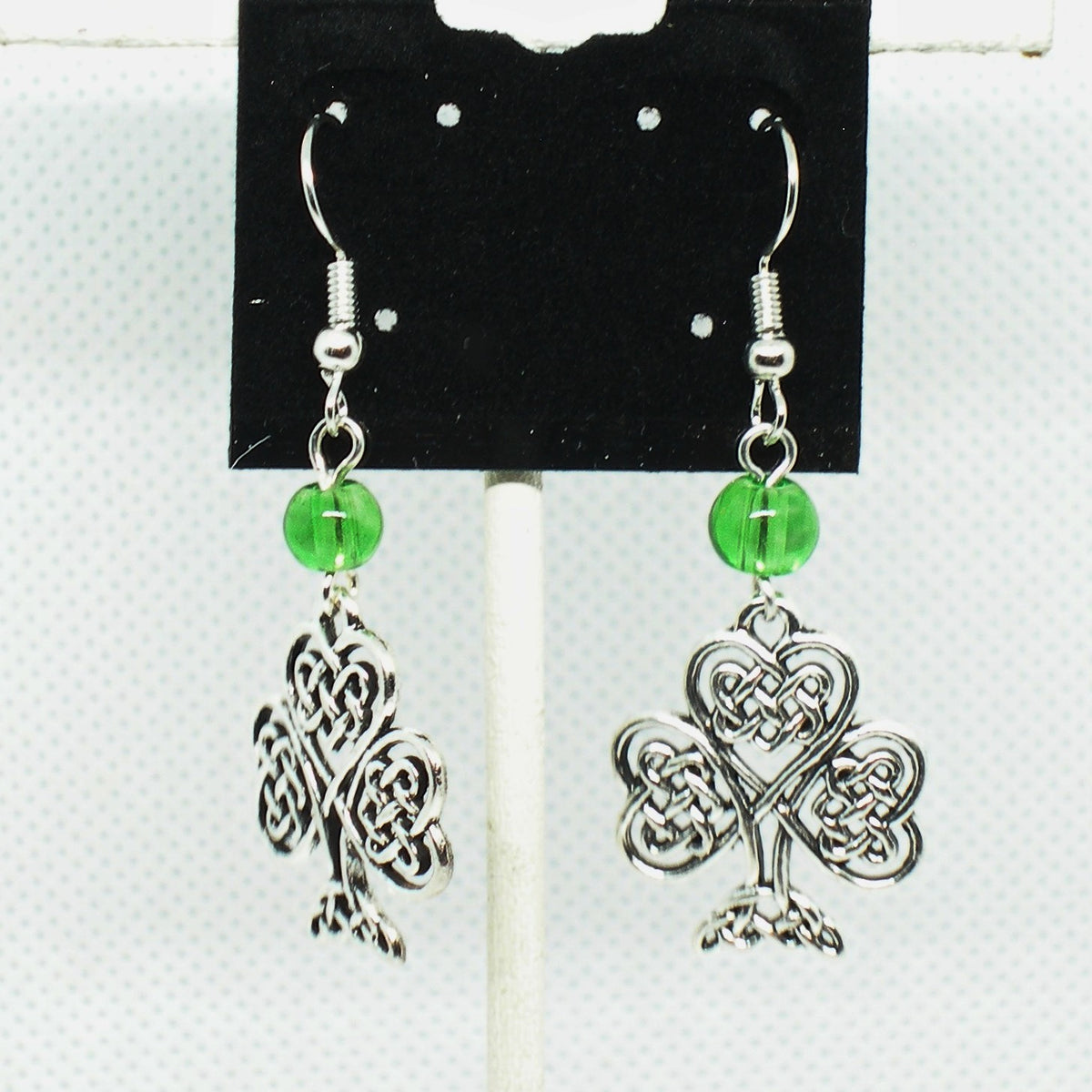 Pair of silver shamrock earrings with green beads on a display card.