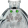 Celtic knot shamrock earrings with green beads on a clear glass bottle.