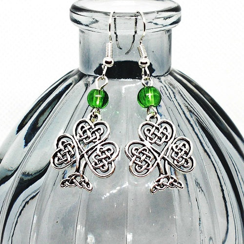 Celtic knot shamrock earrings with green beads on a clear glass bottle.