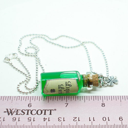 Green bottle necklace with a label on a white background with a ruler for scale.