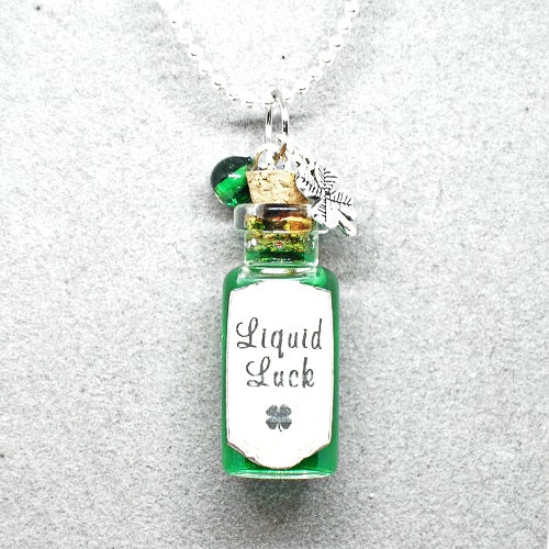 Small bottle labeled 'Liquid Luck' with charms on a textured gray background