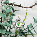 Silver pendant with green design on a branch with leaves